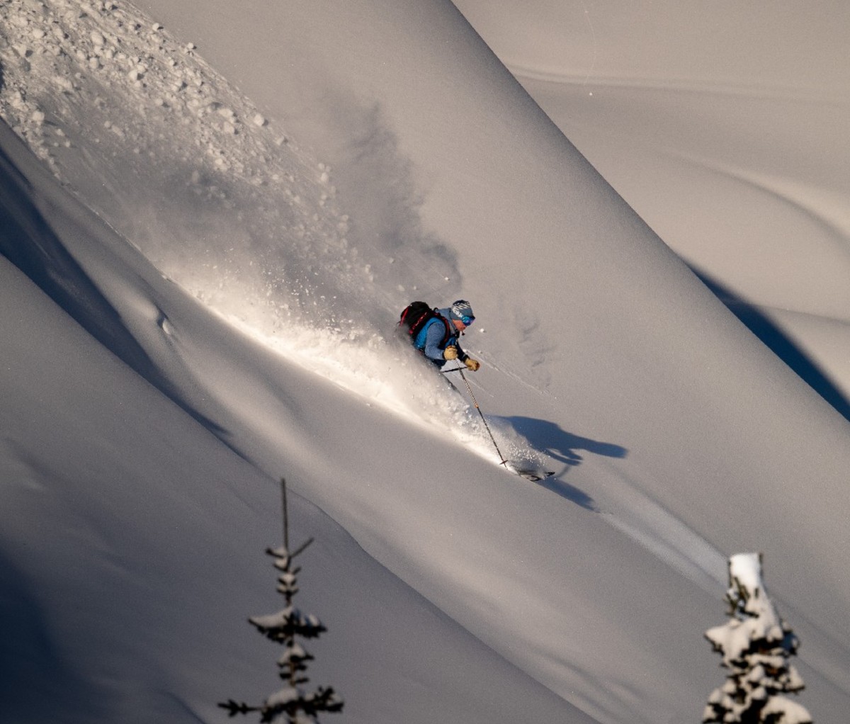 Backcountry skier in BC skiing down a steep, powdery slope.