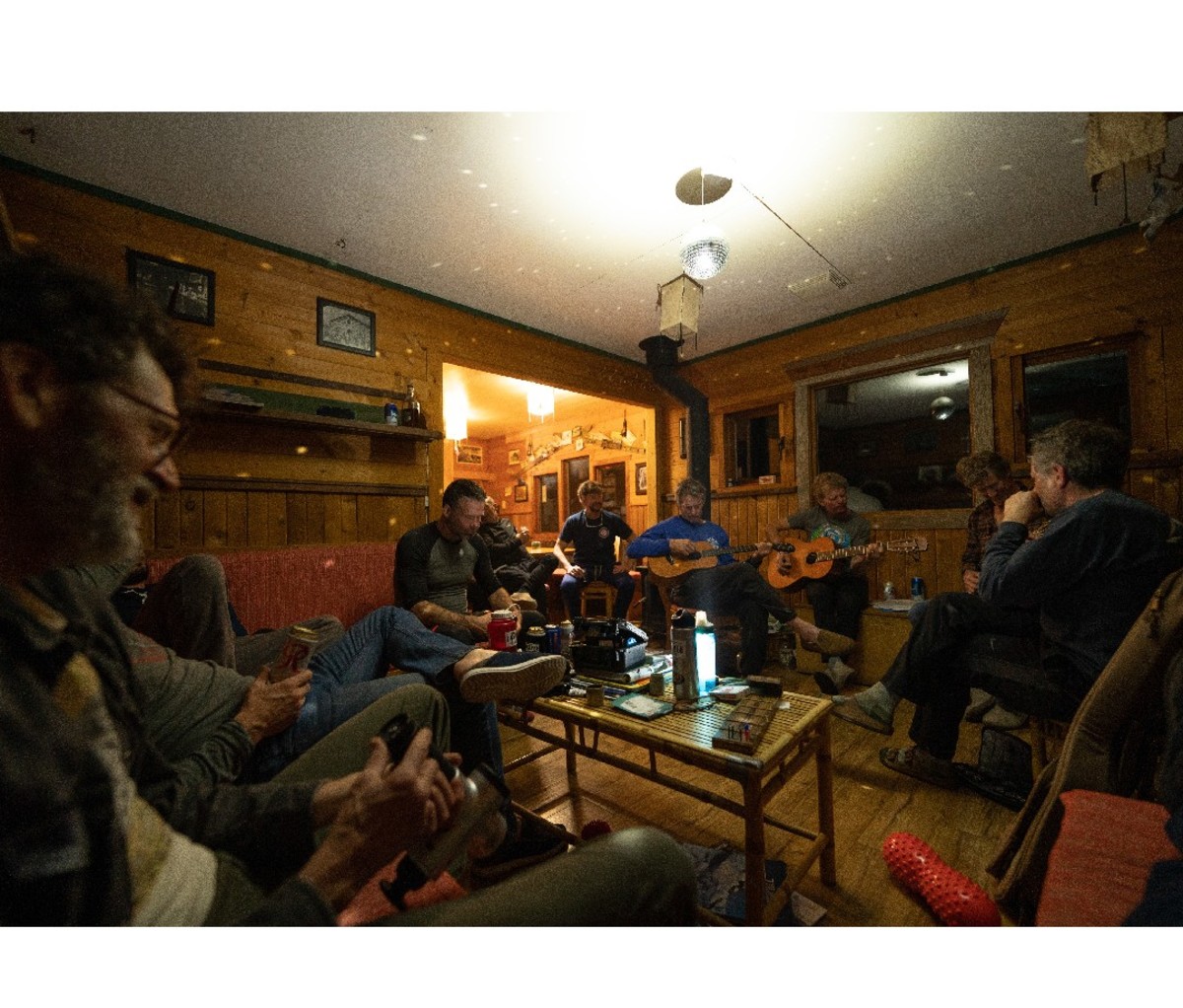 Guests at the Mount Carlyle Backcountry Lodge kick back with drinks and guitars in the living room after a ski day.