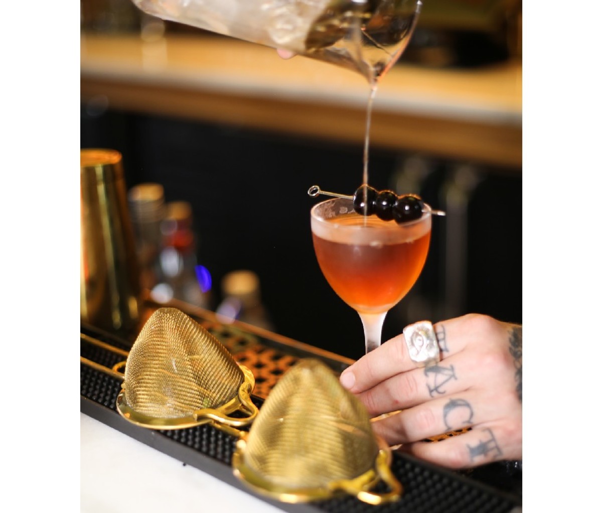 Bartender's tattooed hand pouring a strained drink at Peychaud's bar in New Orleans