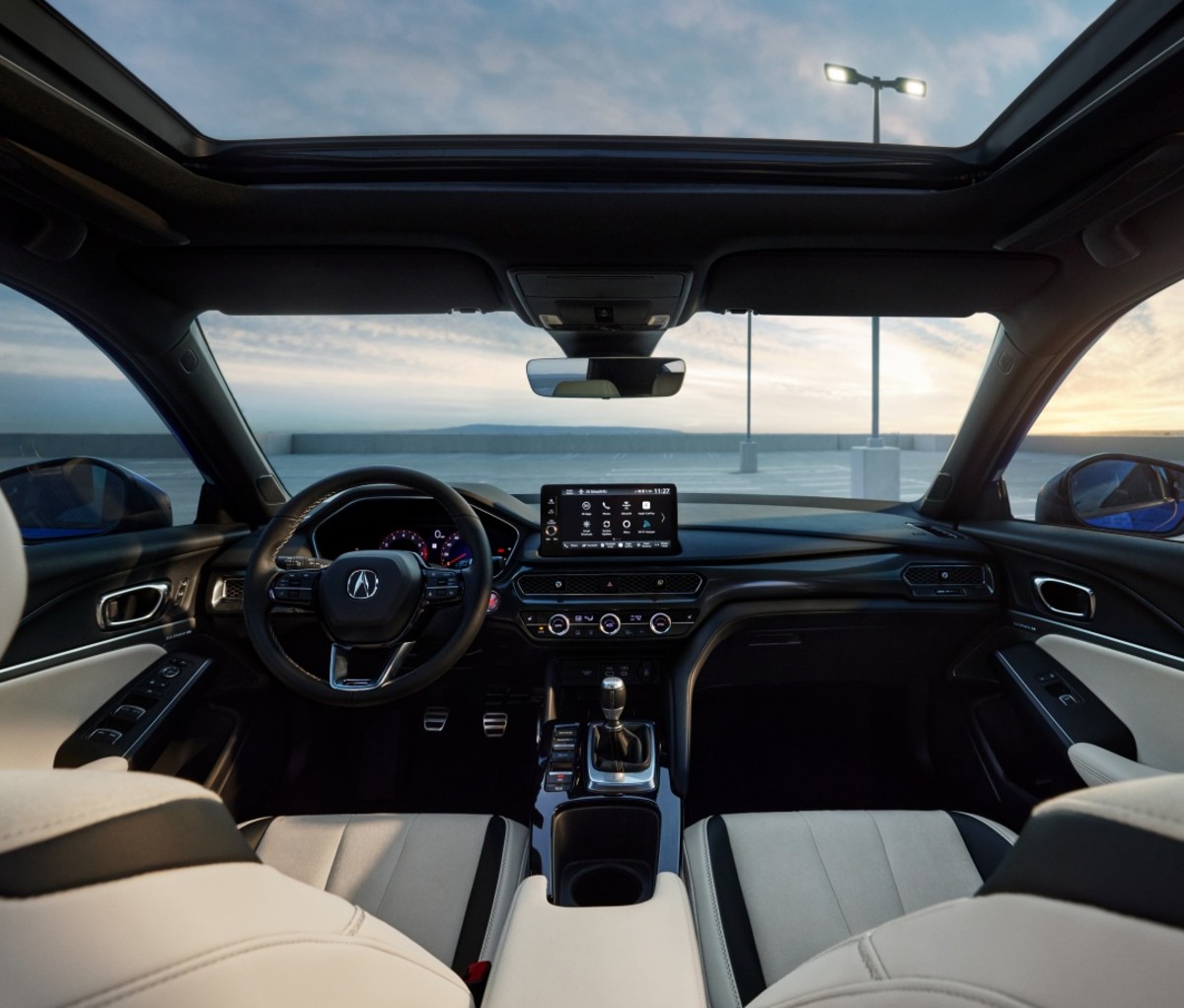 Interior of the 2023 Acura Integra showing the dashboard, gear shifter, steering wheel, windshield, sunroof, and white leather seats