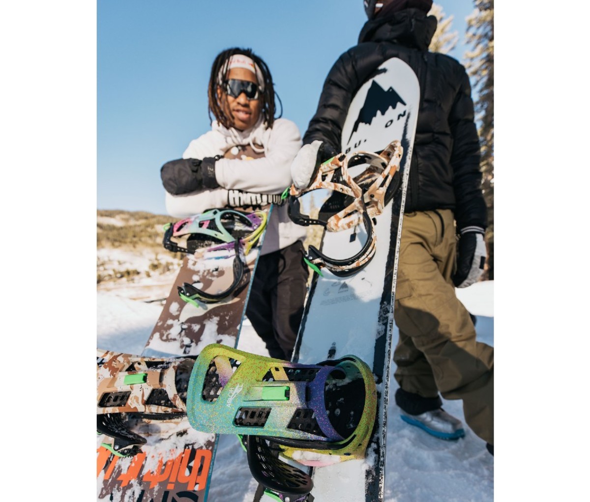 Black man in snowboard gear standing in front of boards