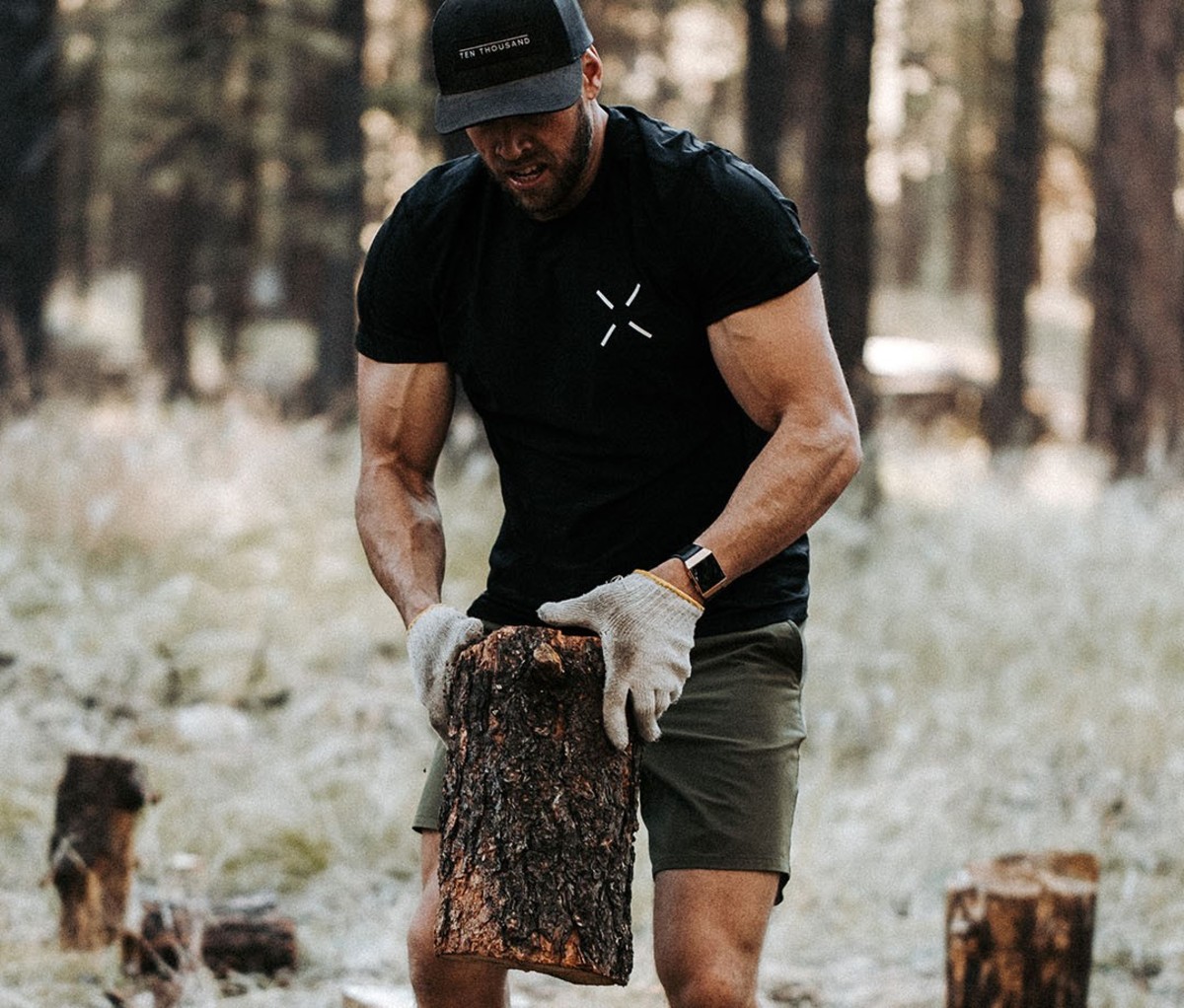 Man wearing black T-shirt chopping wood in gloves