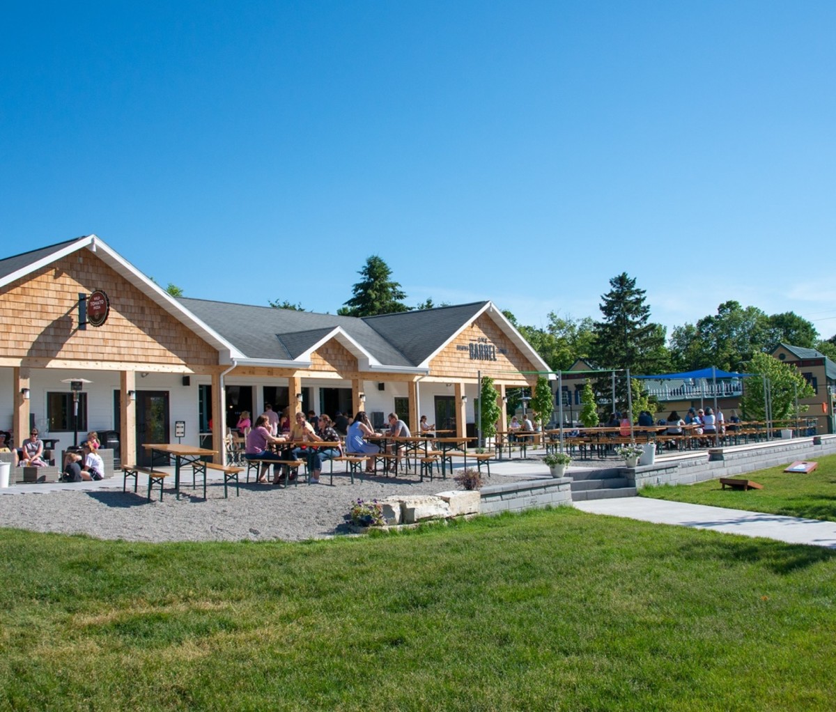 Exterior of One Barrel Brewing Company with a beer garden and people at outdoor tables by a lawn