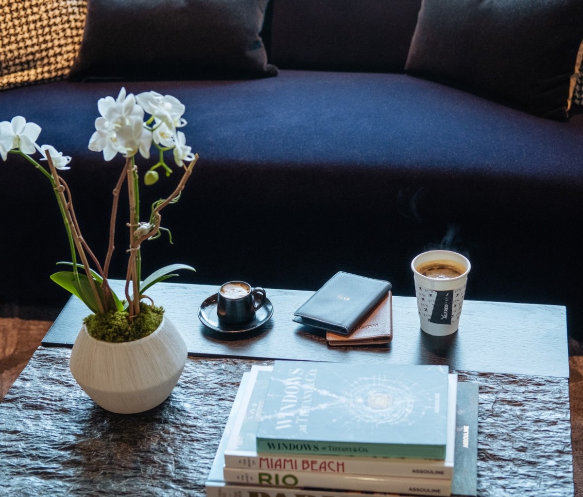 View of PS lounge coffee table with coffee cup and espresso beside books and a vase with flowers