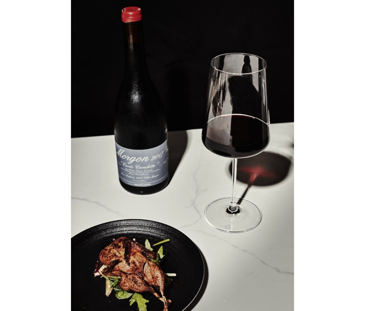 Glass of red wine next to bottle and plate of chicken