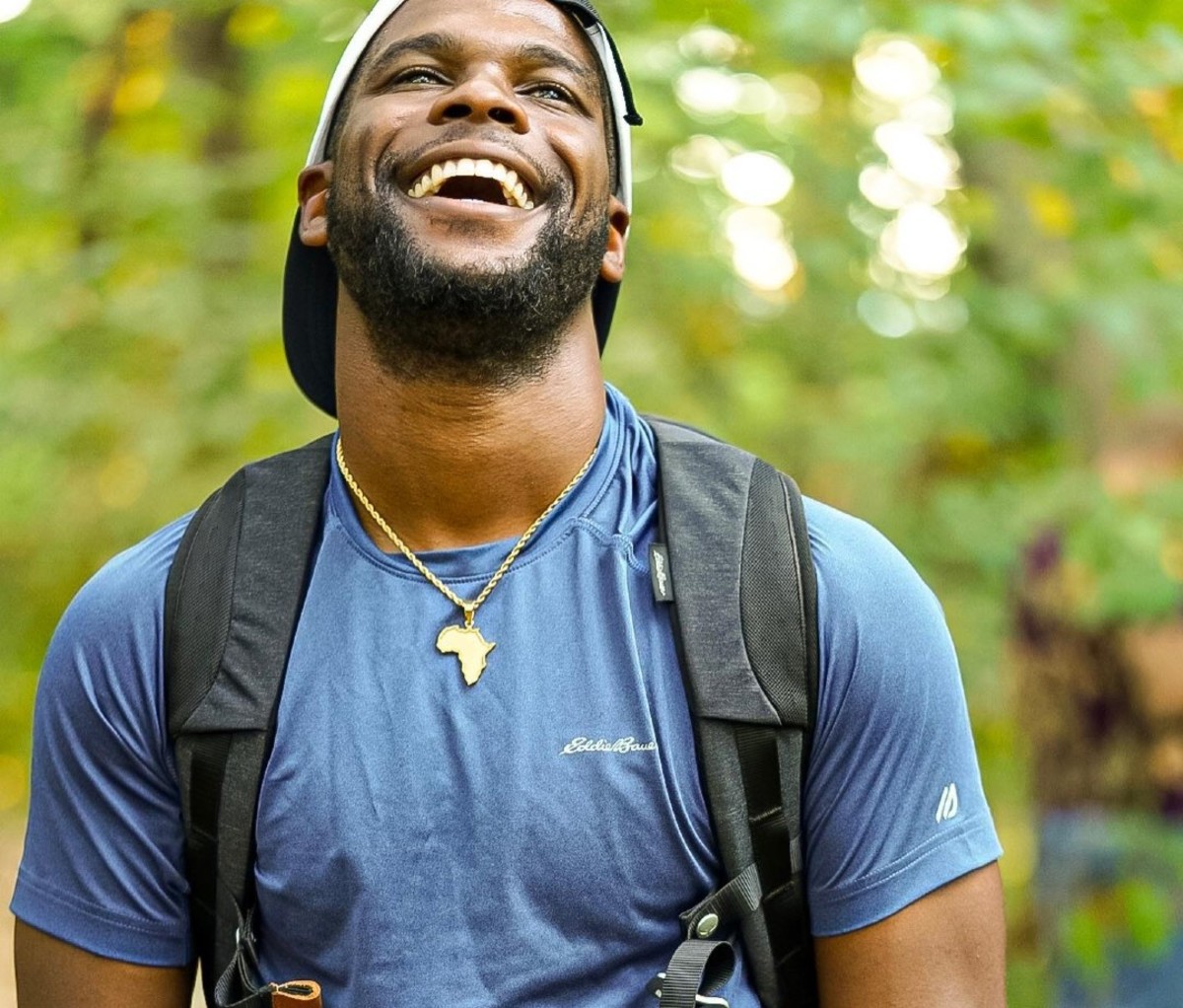 Black man in blue T-shirt and backpack laughing