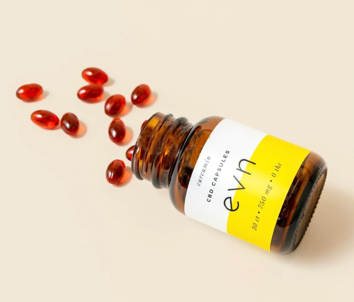 Bottle with white and yellow label on side with orange capsules spilling out