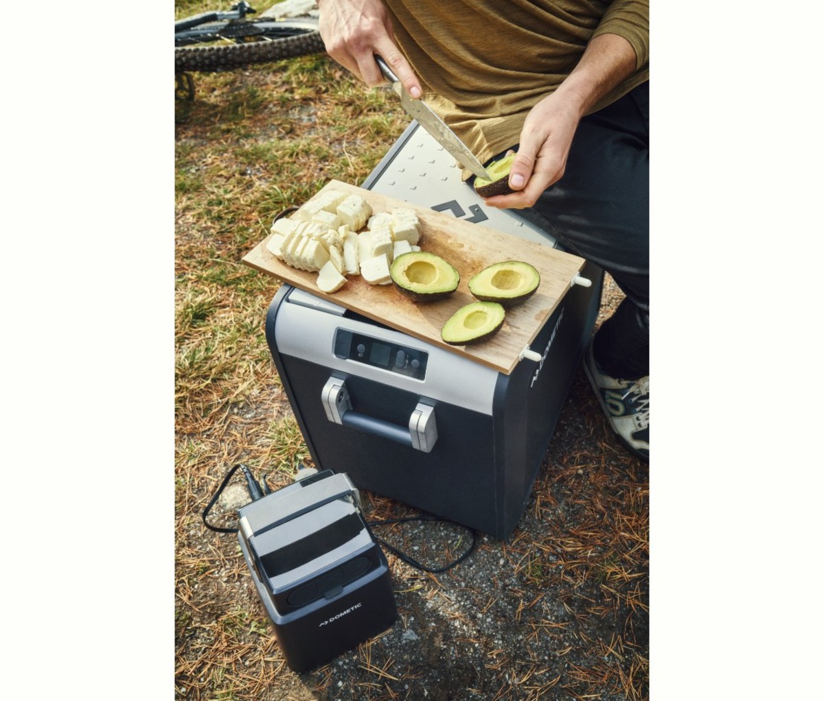 Man sitting on powered cooler with attached battery pack and avocados on cutting board