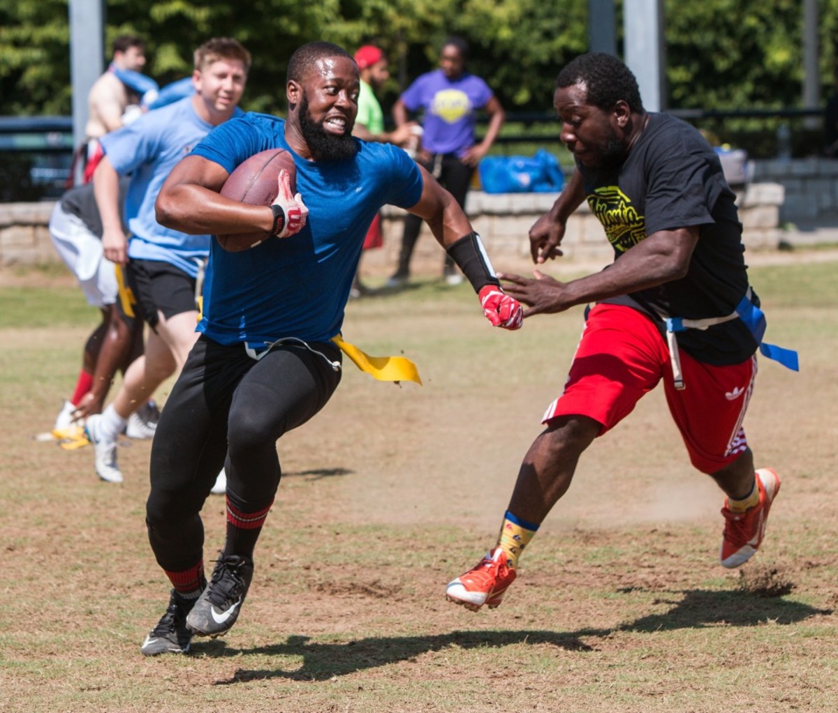 A man carrying the ball runs away from a defender in a recreational flag football game