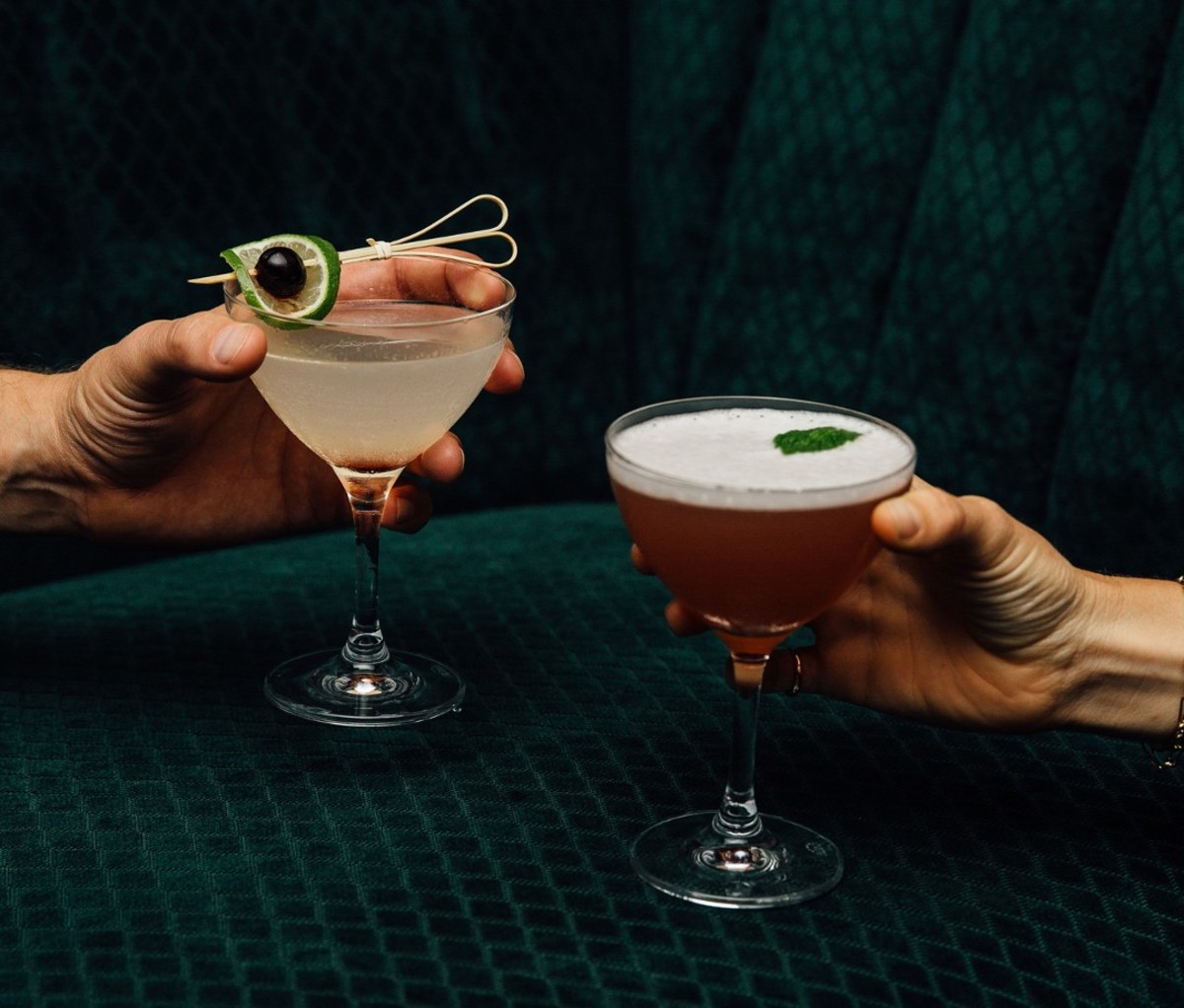Hands holding cocktails against green velvet sofa