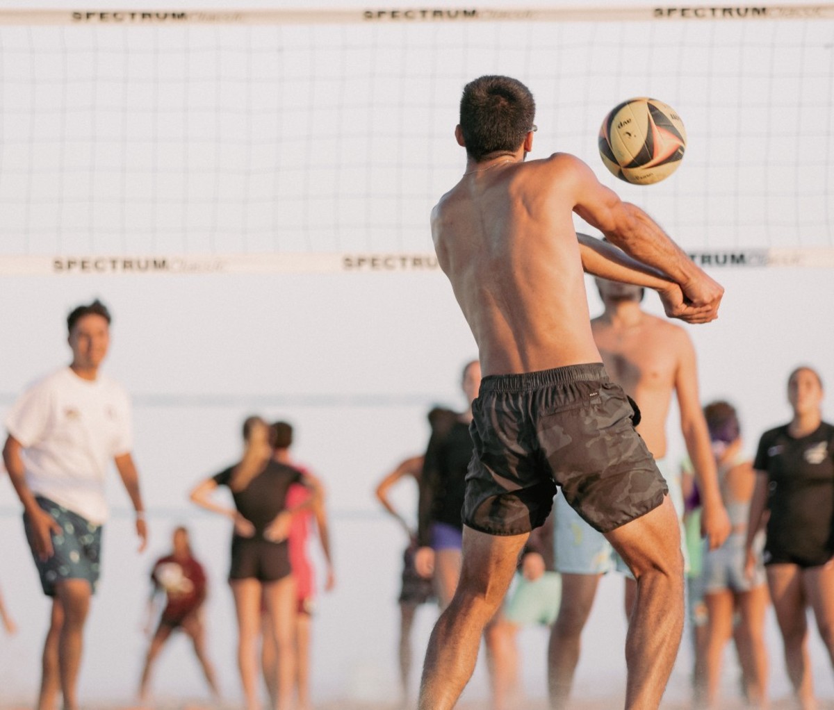 Shirtless man hitting volleyball off forearms at beach