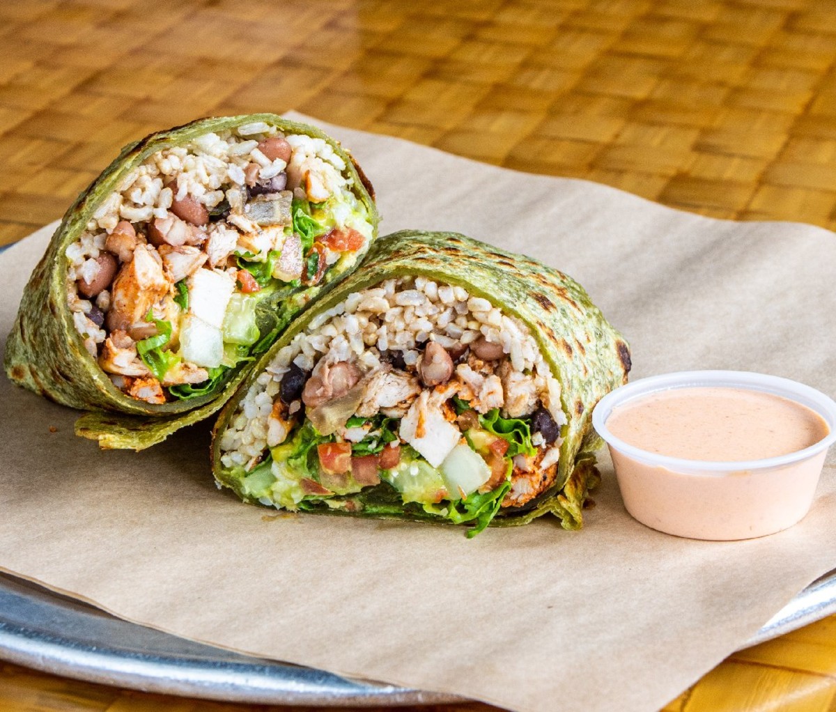 Halved burrito on a plate with green spinach tortilla from Cabo Bob's Burritos