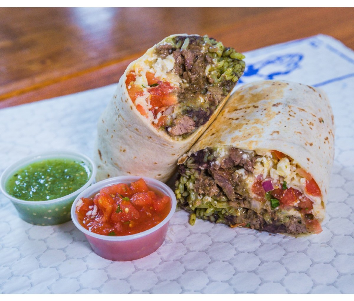 Halved burrito on a plate with green and red salsa at Coyo Taco