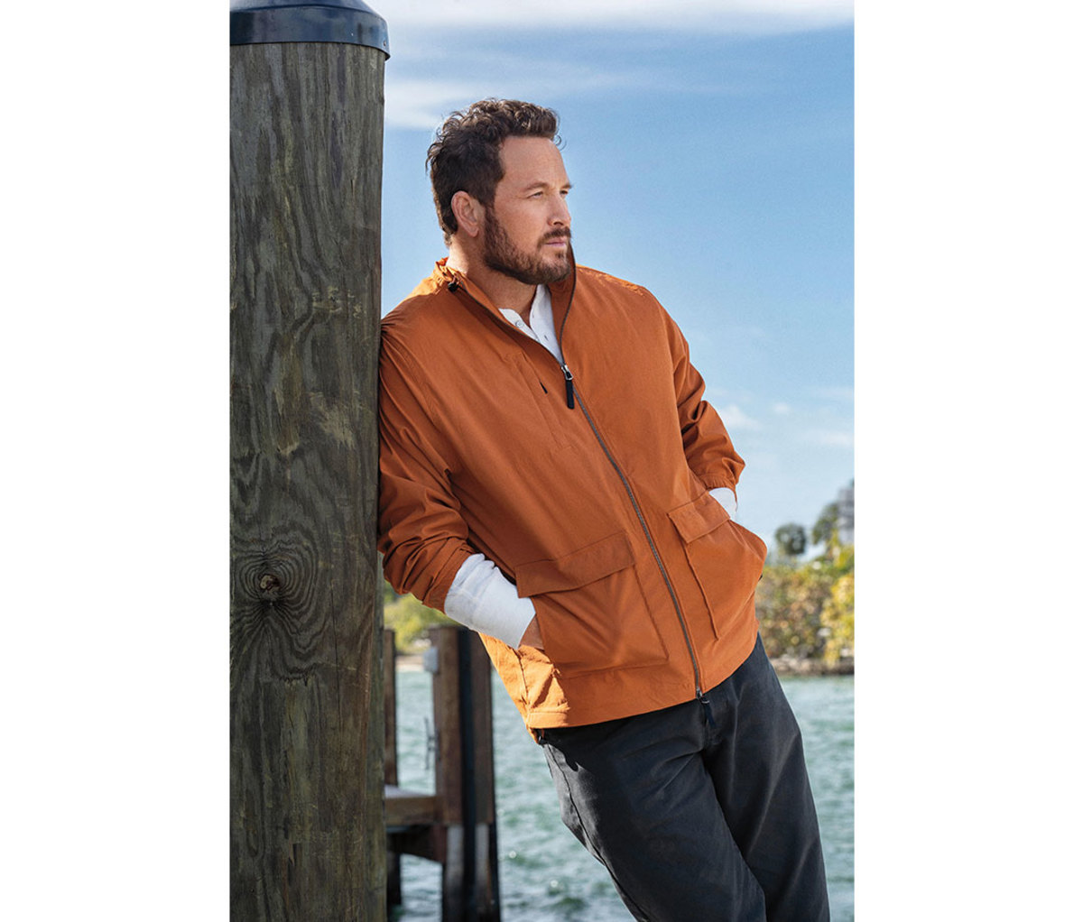 Caucasian man in orange jacket leaning against pier