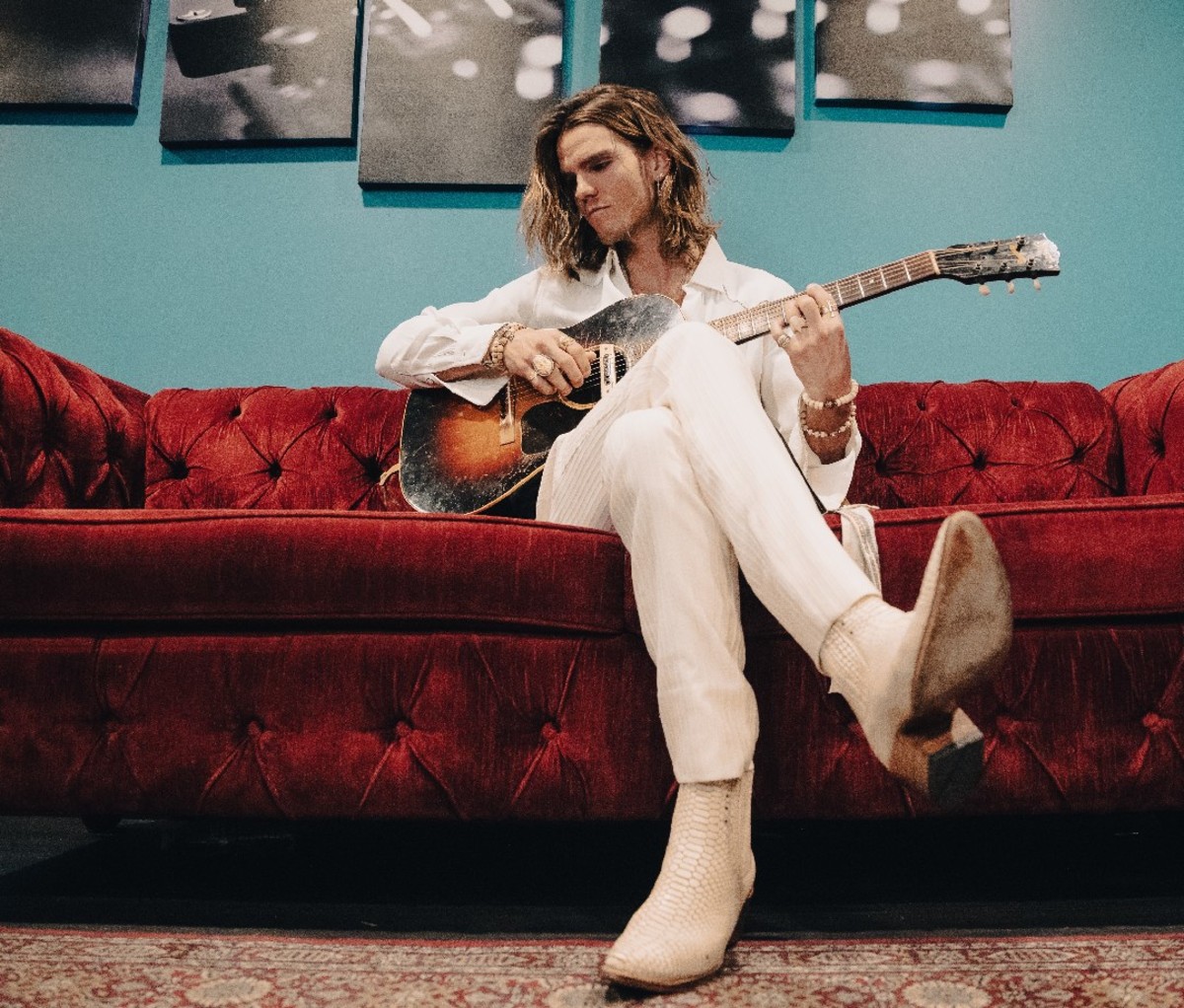 JJ Julius Son sitting on a red couch with guitar in hand.