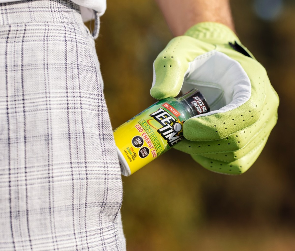 Man in plaid shorts and golf glove holding energy shot