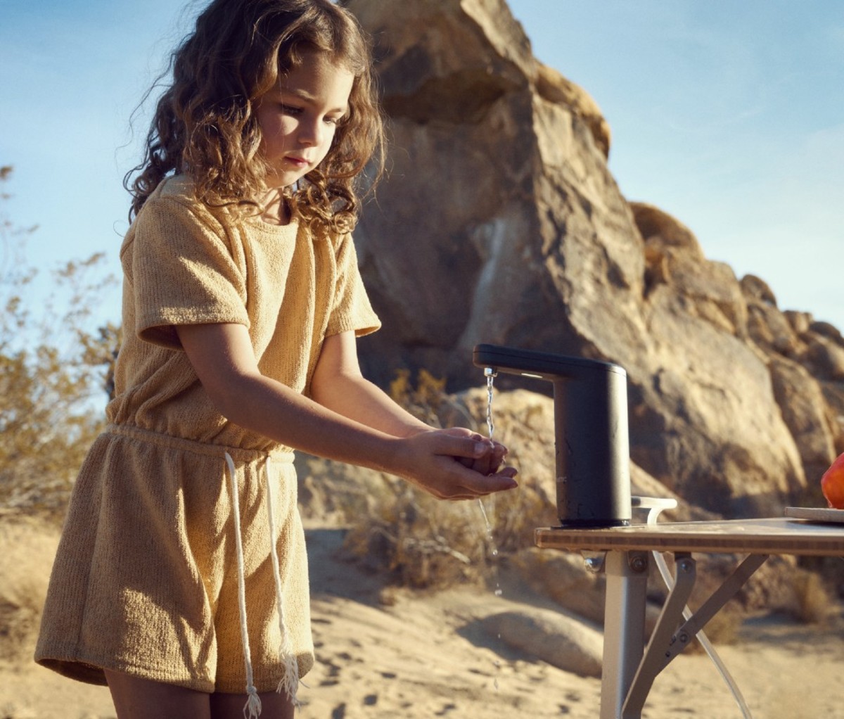 Little caucasian girl with brown curly hair using portable faucet to wash hands