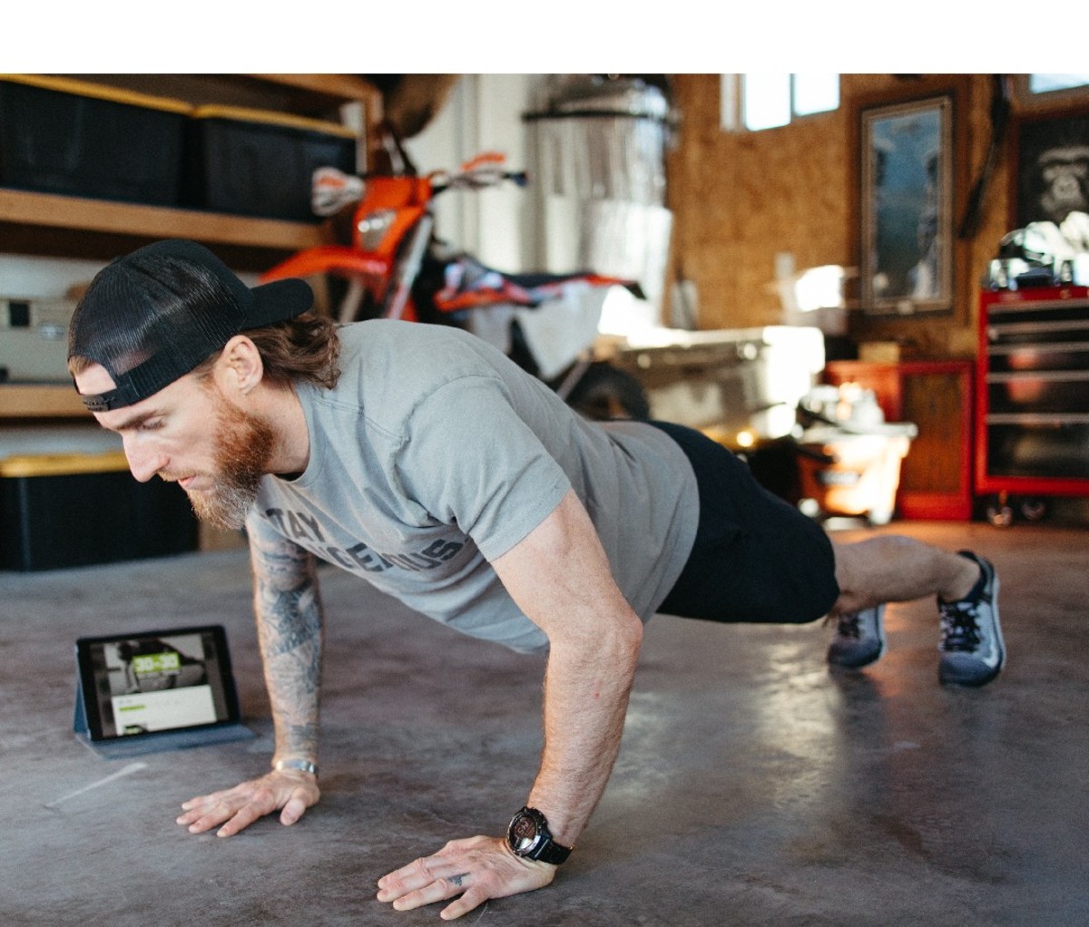 Guy in push up position in garage with tablet on background.