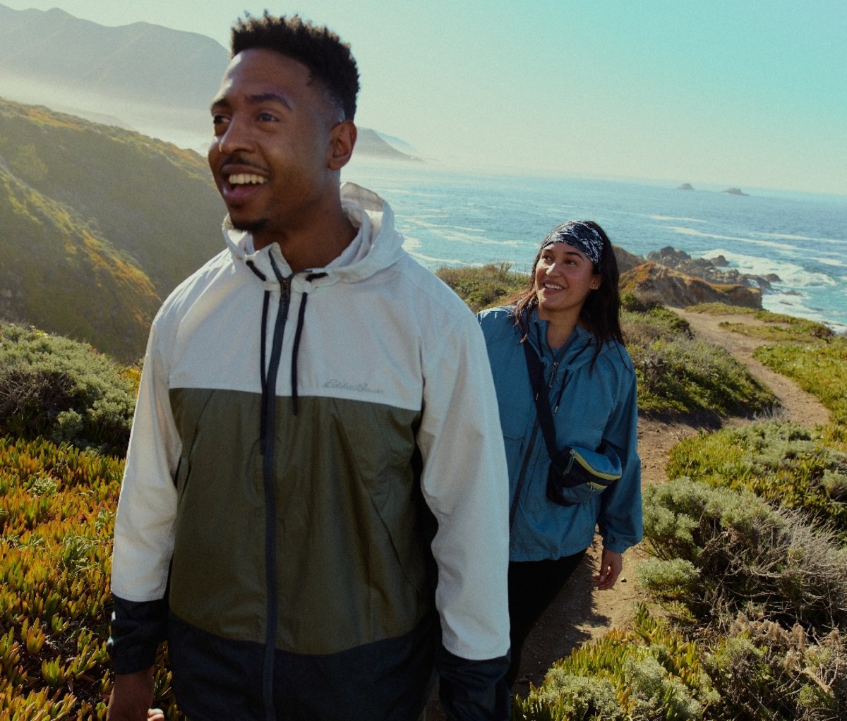 Two hikers smiling while walking along a coastal trail
