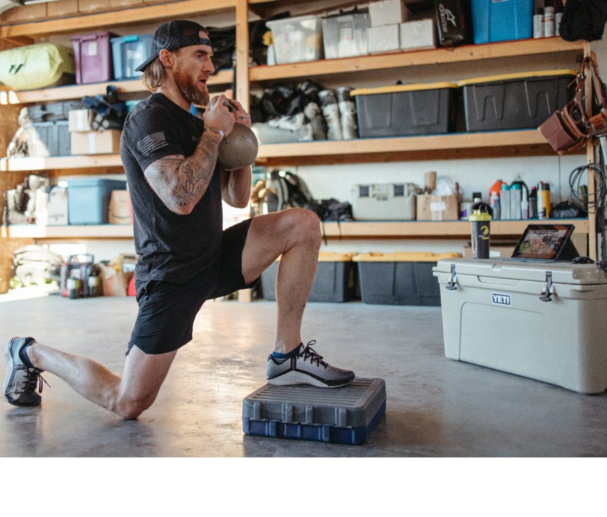 Guy doing kettle bell excercise in garage, with tablet propped up on a cooler