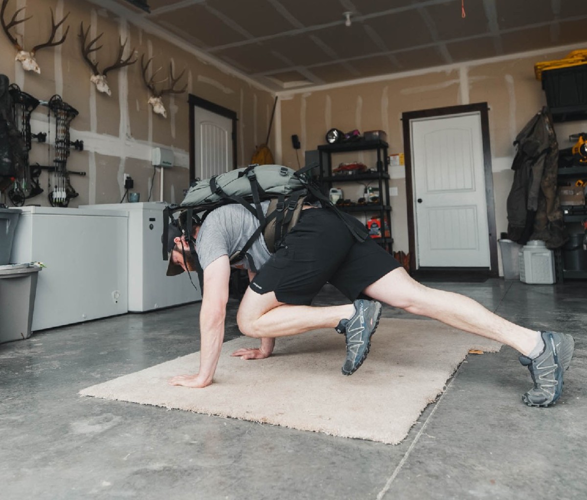 Guy exercising in garage with backpack in forward stretch position.