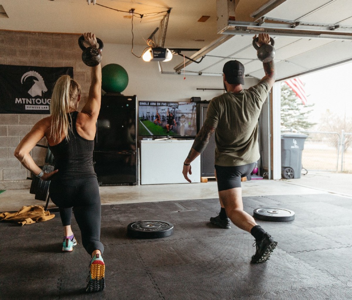 Woman and man in garage doing tandem kettle bell exercise.