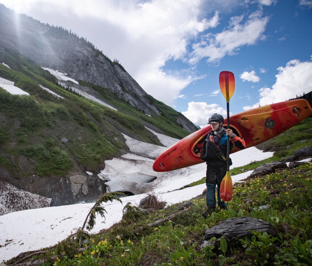 Kayaker carrying orange kayak and paddle with glacier in background