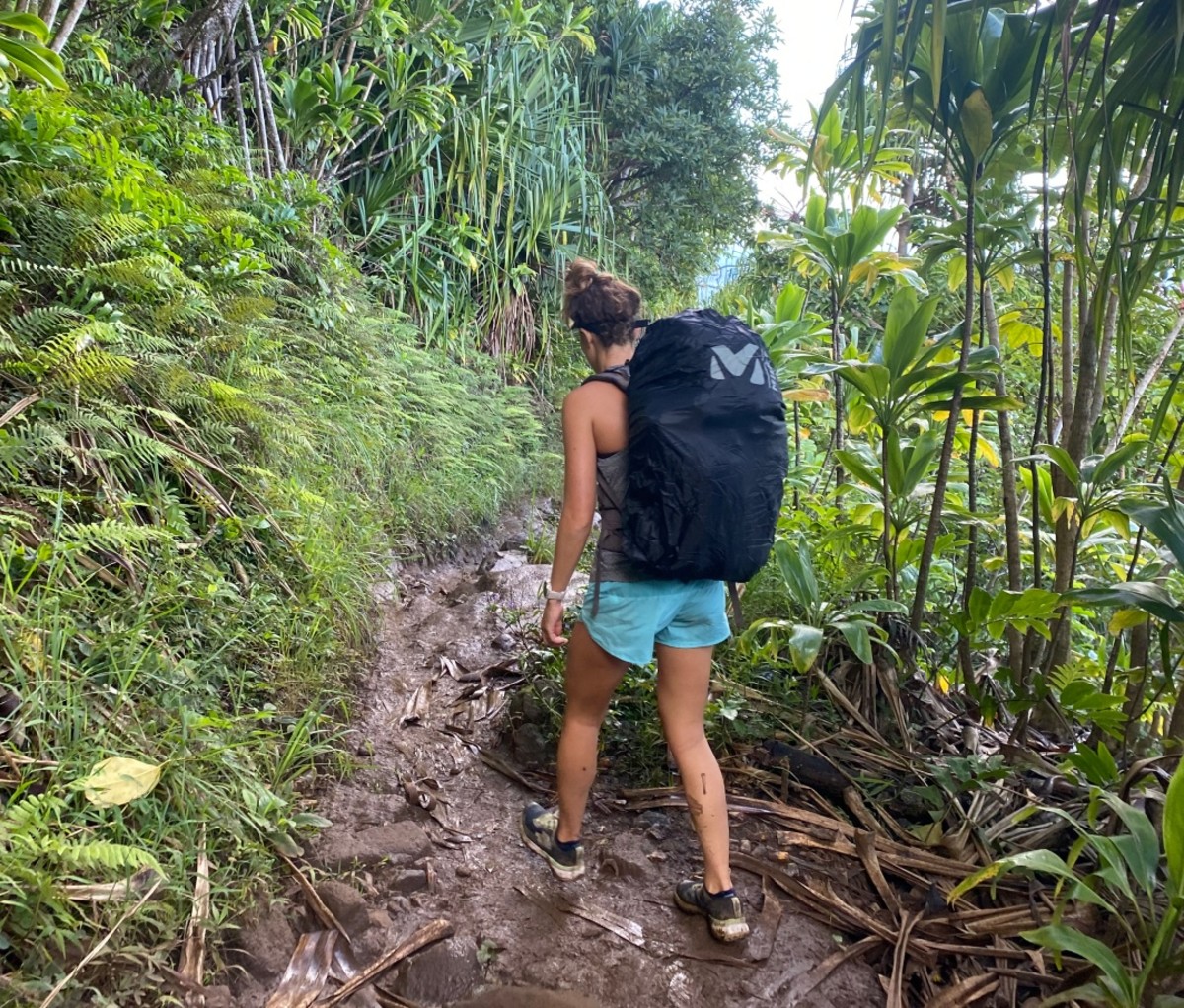 Woman wearing green shorts and a black backpack hiking on a muddy jungle path. Thru-hike