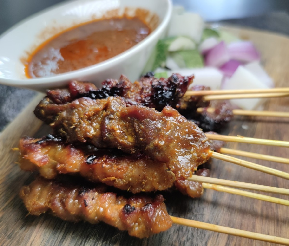 Satay skewers arranged on a plate next to a bowl of dipping sauce. Urban Hawker