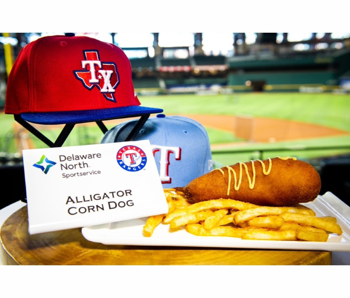 Corn dog with French fries on late with baseball hats and stadium in background