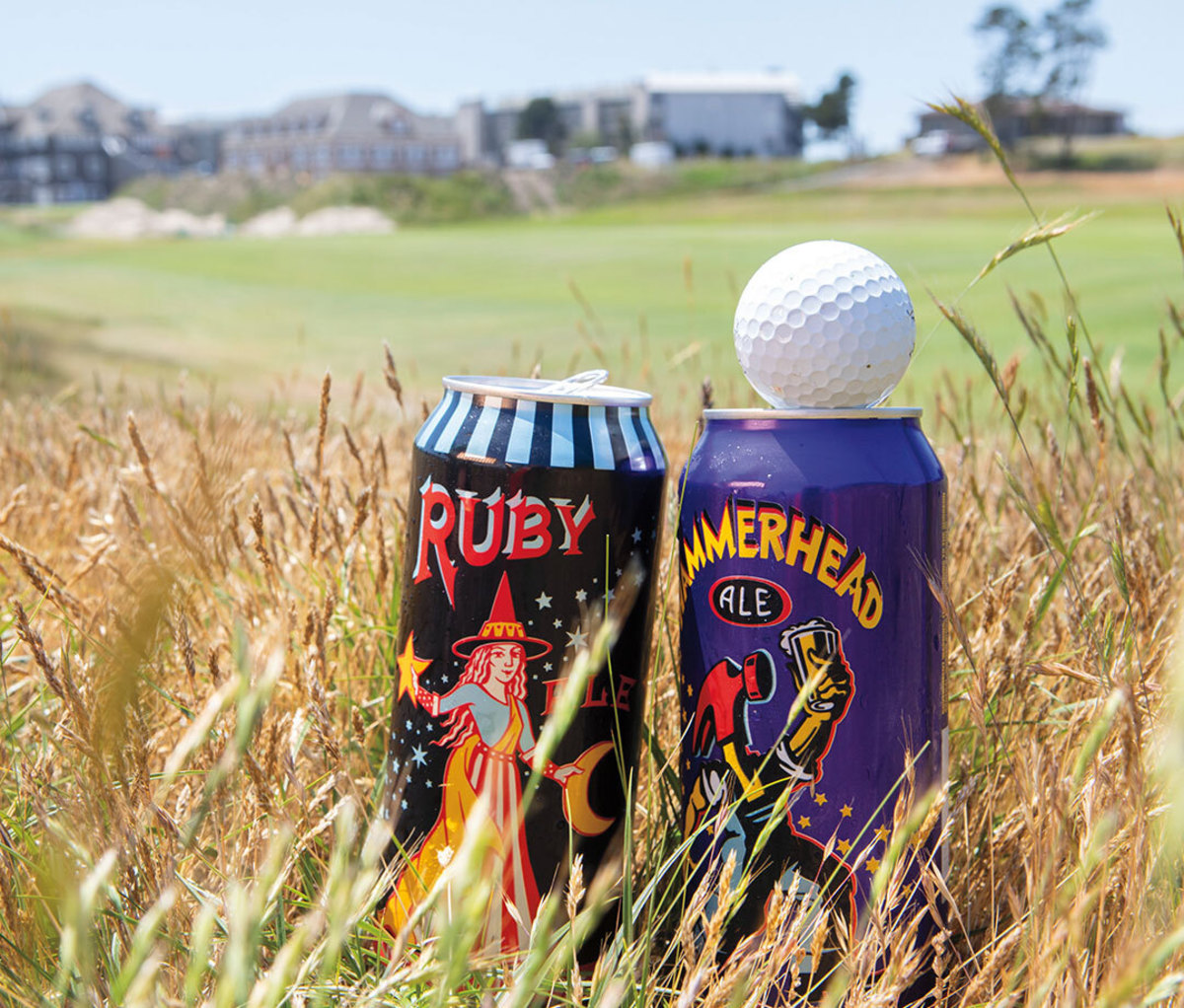 Two cans of beer resting in grass at golf course with golf ball on top of right can