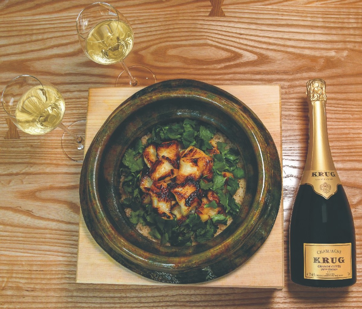 Bottle of Champagne and two filled glasses beside a plate of black cod and saikyo miso rice