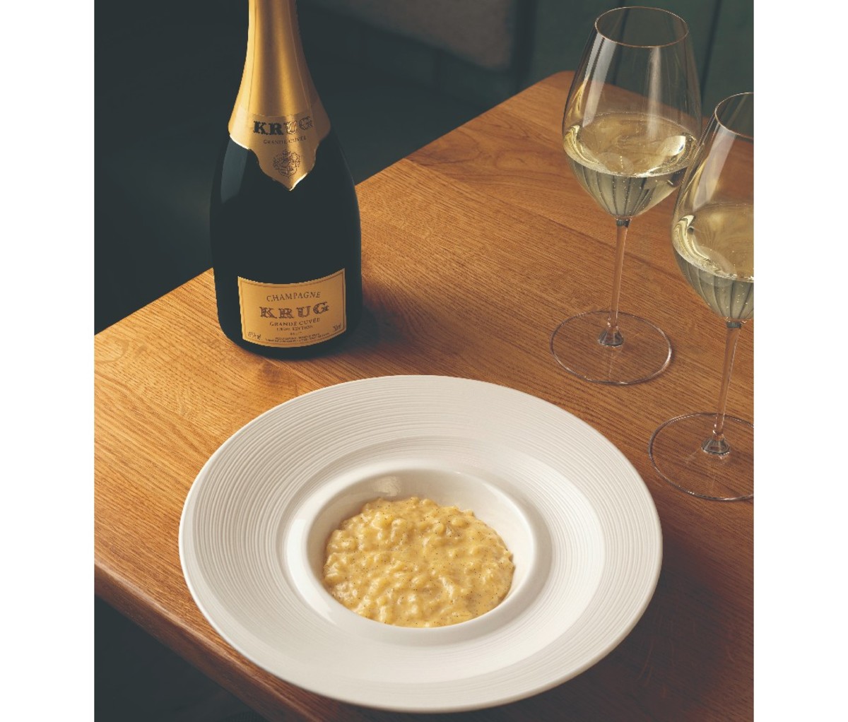 Bottle of Champagne and two filled glasses on a table beside a bowl of rice pudding.