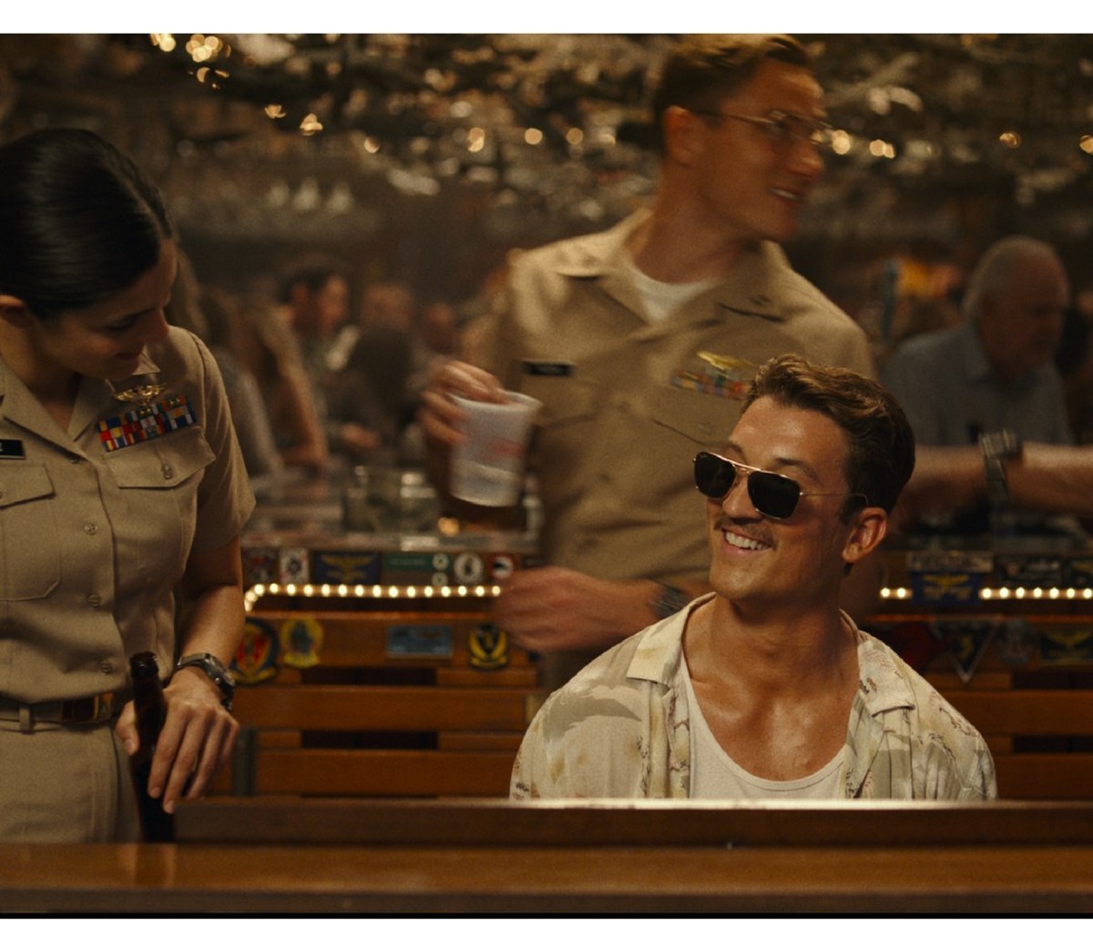 Miles Teller in shades sits at the piano during a scene from Top Gun: Maverick