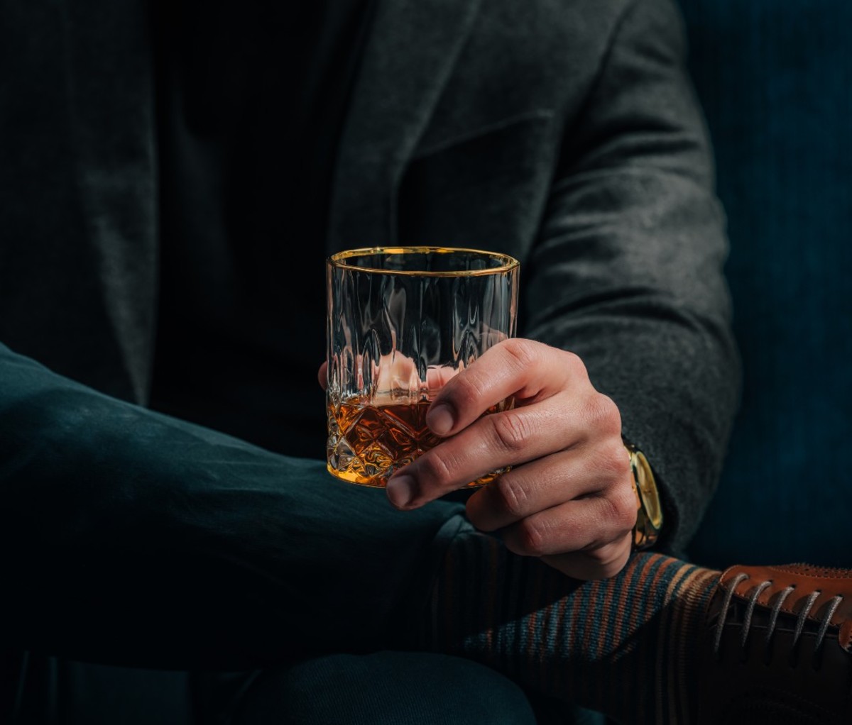 Close-up of caucasian man dressed in sports coat holding dram of whiskey