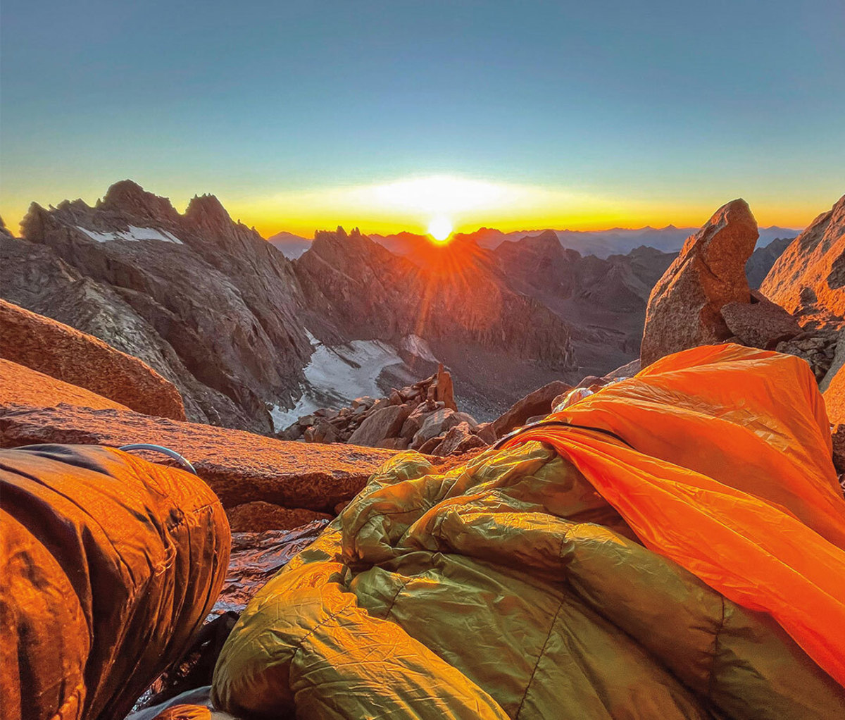 Mountain peaks at sunrise from vantage point of alpinist in sleeping bag