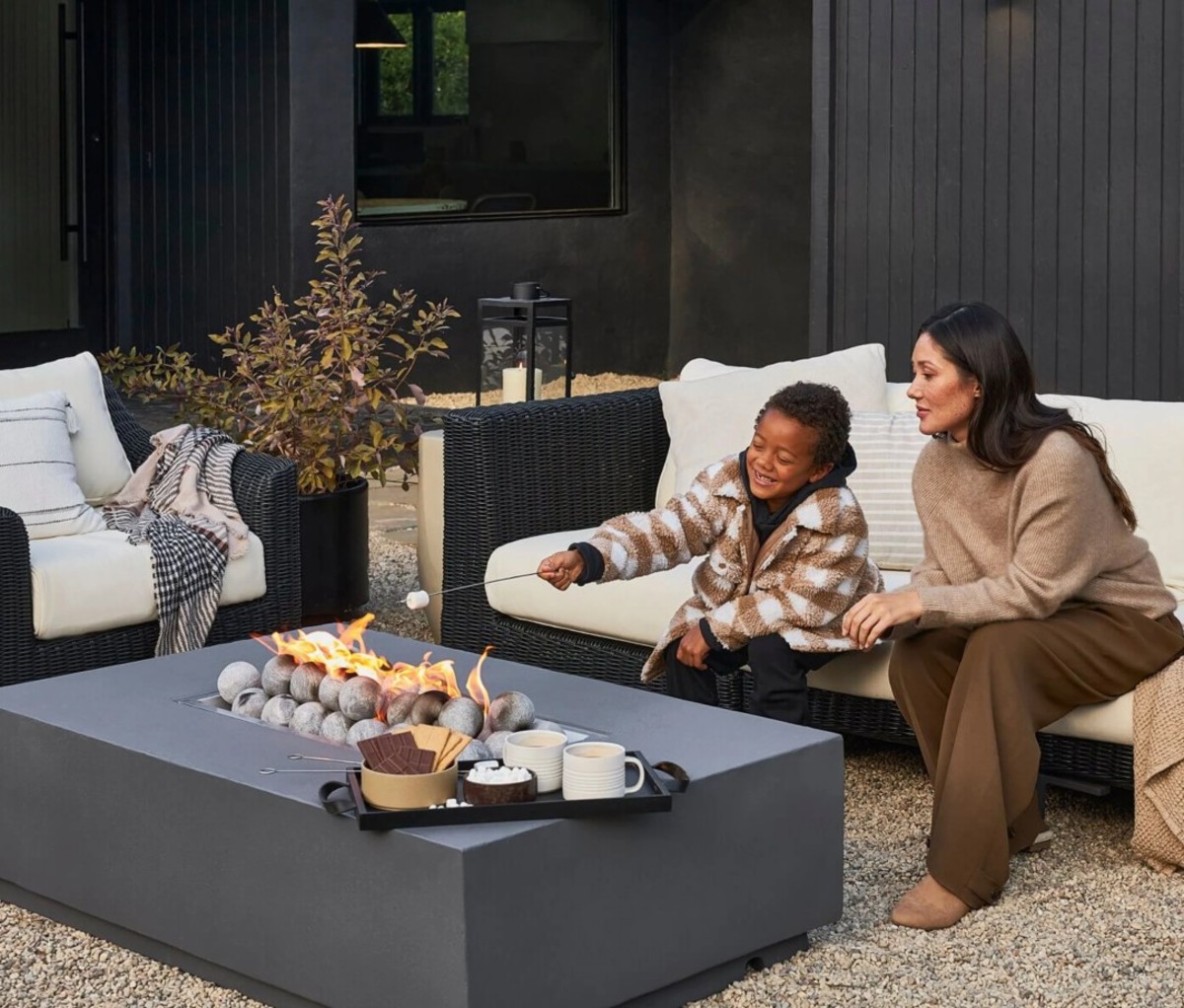 Mother and son sitting on outdoor sofa roasting marshmallow over fire pit