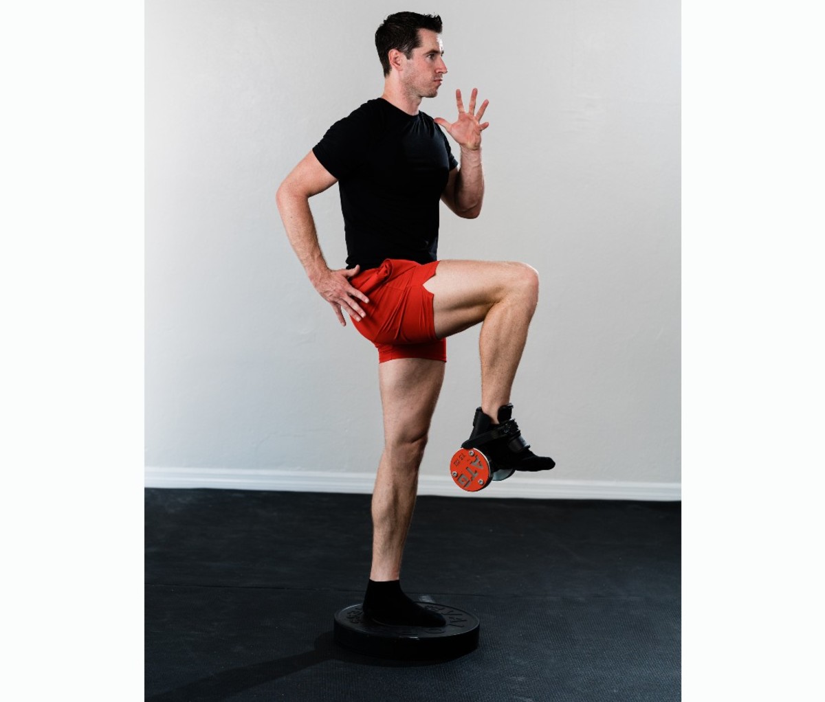 Caucasian man in black t-shirt and red shorts doing hip flexor raise