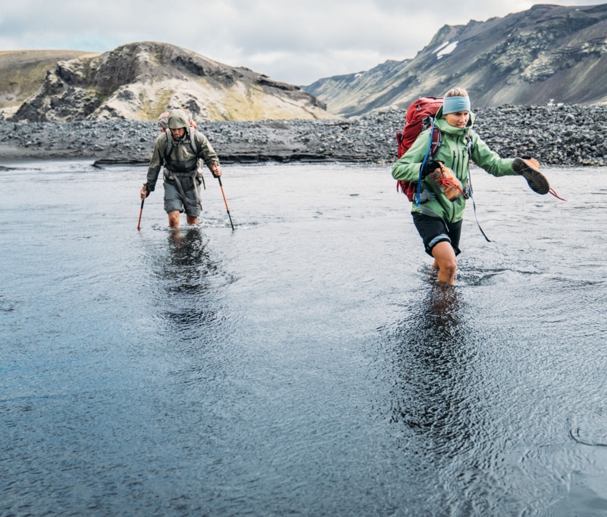 Two people in hiking gear crossing a river in Iceland.