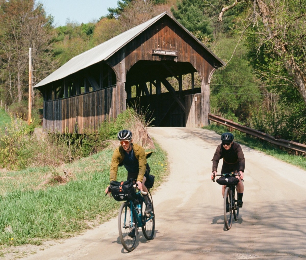 Two cyclists riding on a gravel road near a covered bridge. new england bikepacking