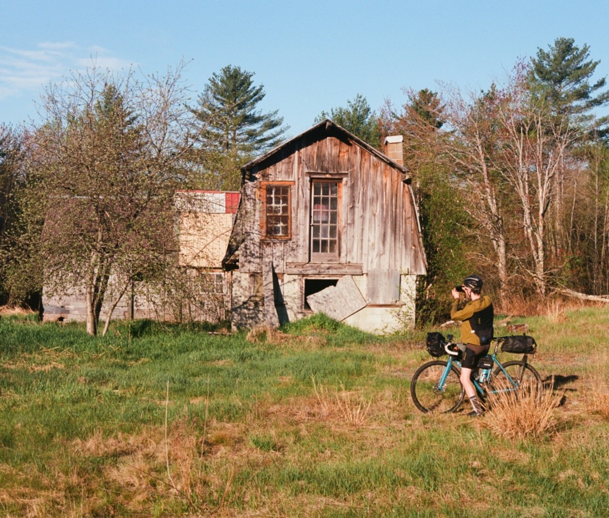 Cyclist in a field by a barn taking a photo with his phone. new england bikepacking