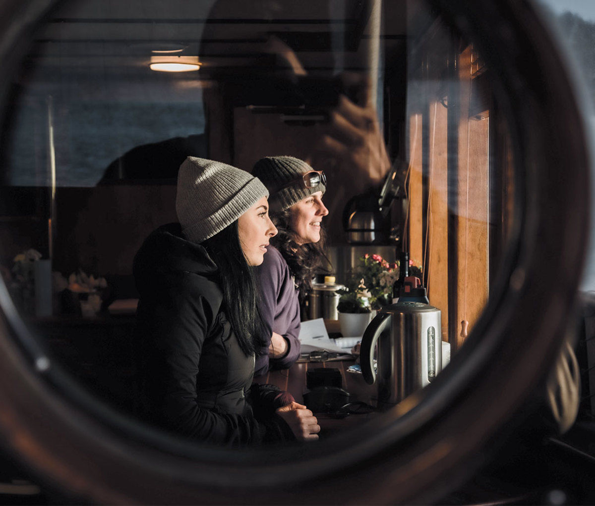 Two women looking out window through porthole