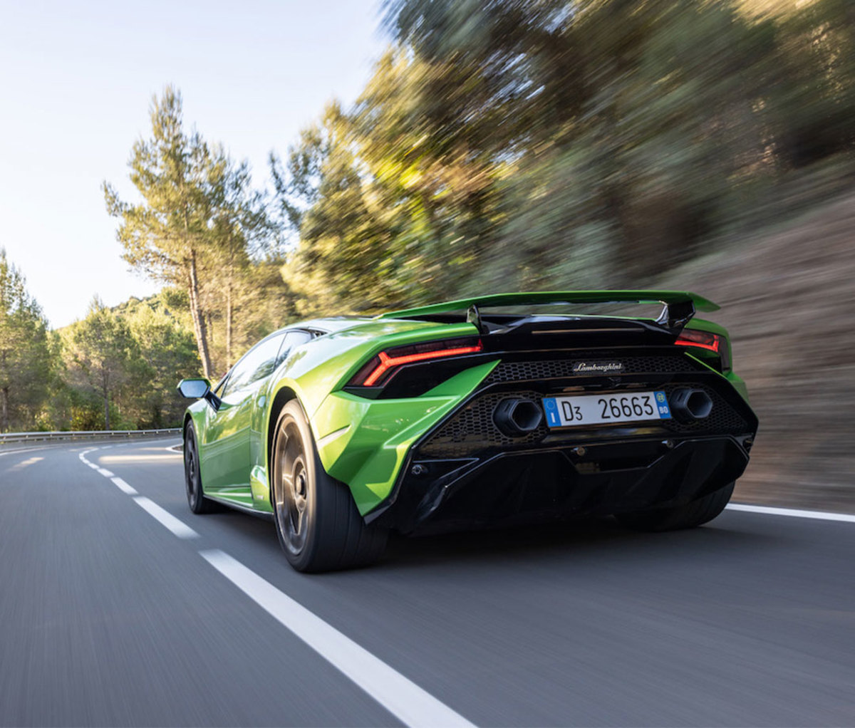 Green sports car on winding road going fast, blurring by trees