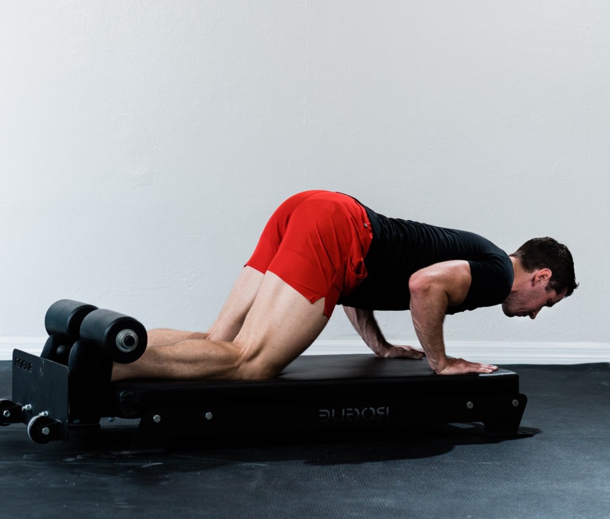 Caucasian man in black t-shirt and red shorts doing nordic hamstring curls