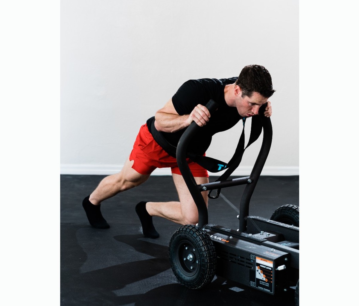 Caucasian man in black T-shirt and red shorts pushing sled