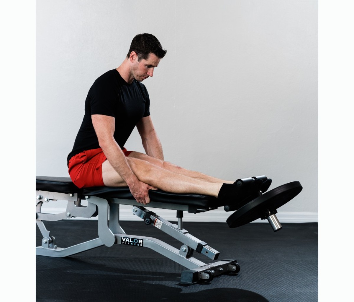 Caucasian man in black T-shirt and red shorts doing tibialis raise on bemch