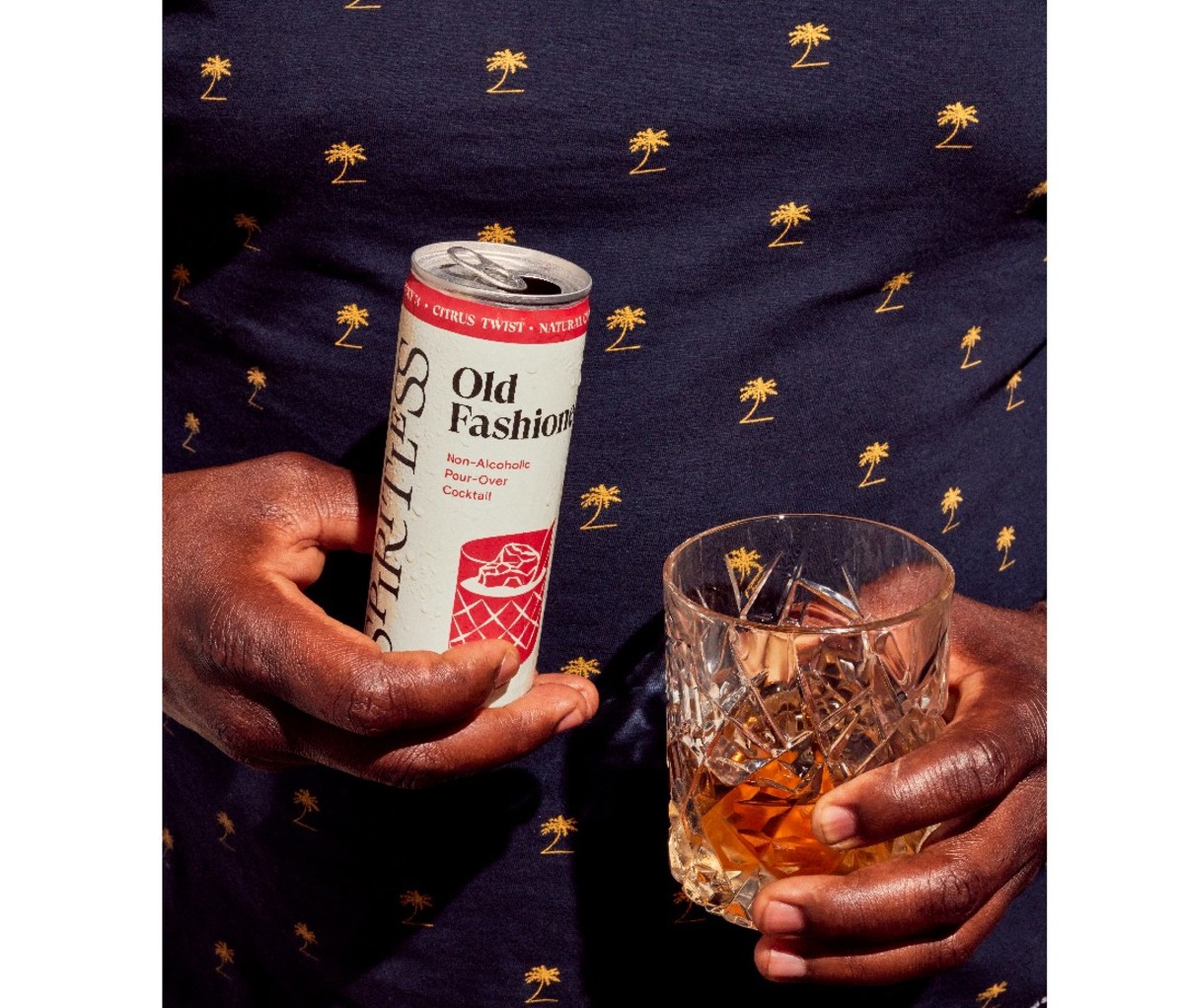 Man holding an open can of Spiritless Whiskey Cocktails poured into a rocks glass.