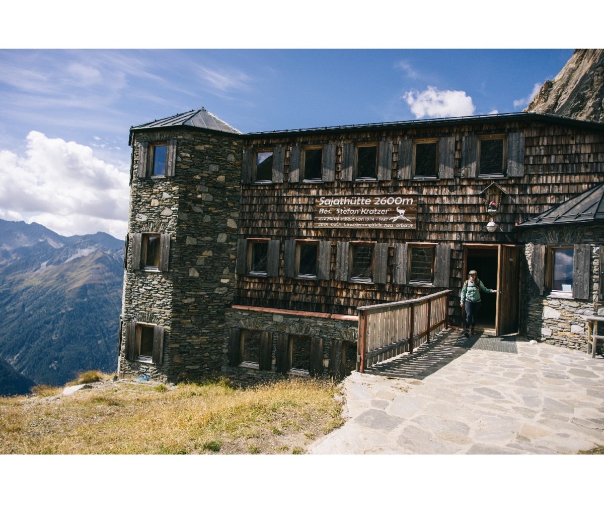 Hiker walking out of rustic accommodations in the mountains along Austria's Eagle Way.