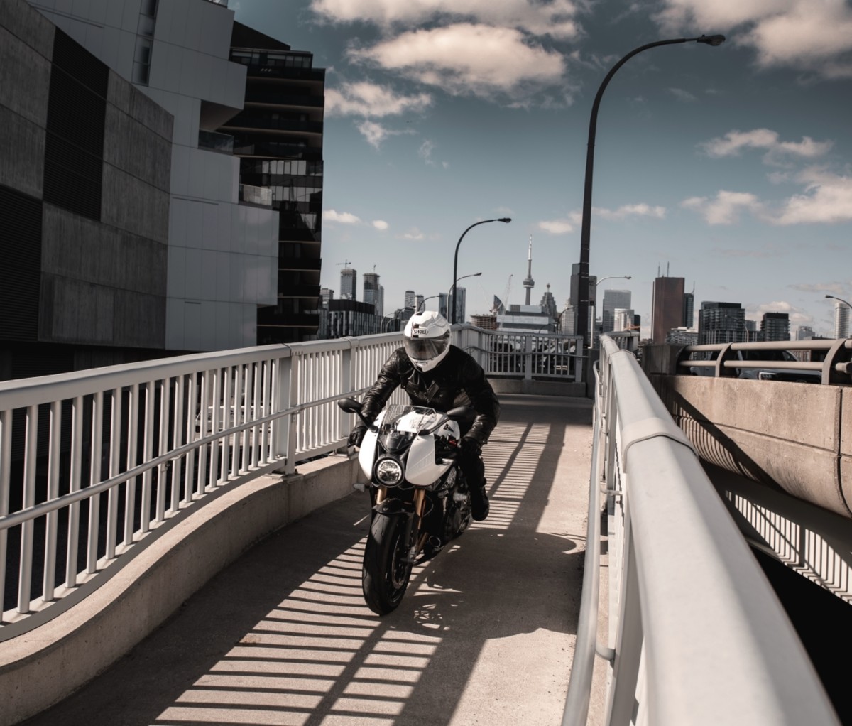 Person riding a Triumph Speed Triple 1200 RR on a narrow bridge in a city.