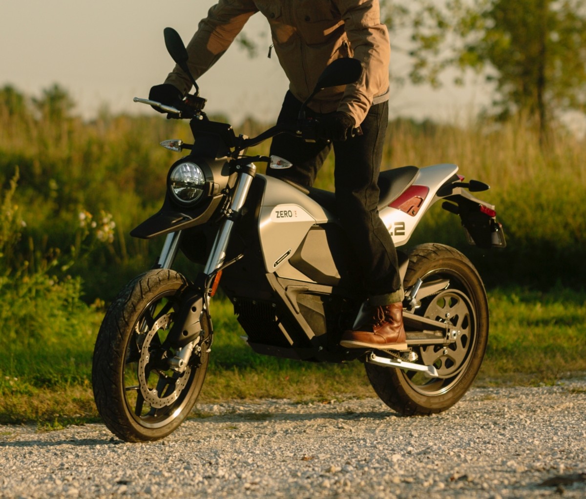 Man riding a Zero FXE motorcycle on a gravel road.